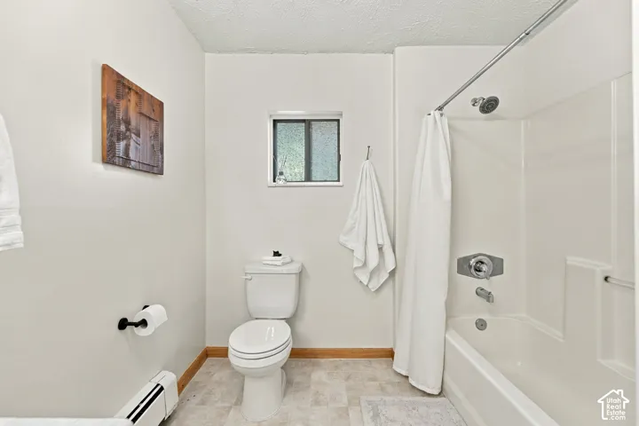 Bathroom featuring a white integrated tub and shower surround, chrome fixtures, a low-profile toilet, and window with textured glass
