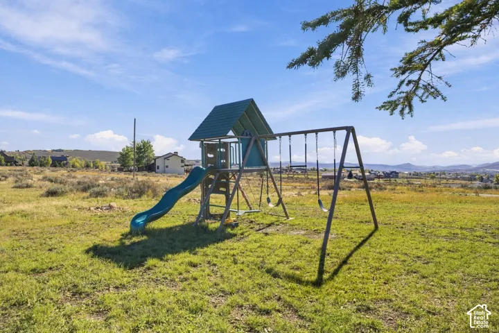 Expansive open lot featuring native grasses and a built-in metal and plastic play structure with a slide and swing set