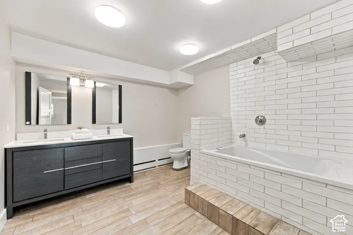 Double vanity with integrated rectangular sinks, white subway tile tub surround, built-in soaking tub, wood-finish flooring, and dual framed mirrors