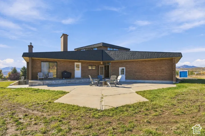Exterior featuring brick masonry, expansive concrete patio, two masonry chimneys, and multi-faceted roofline with mountain backdrop
