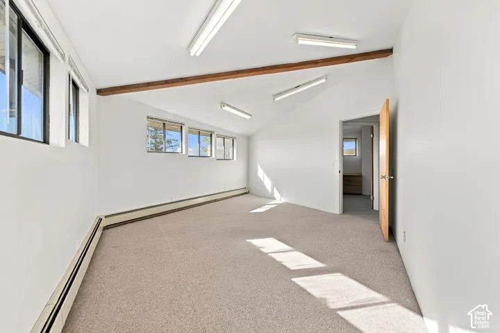 Vaulted ceiling featuring exposed wood beams, wall-to-wall carpeting, and linear fluorescent lighting fixtures