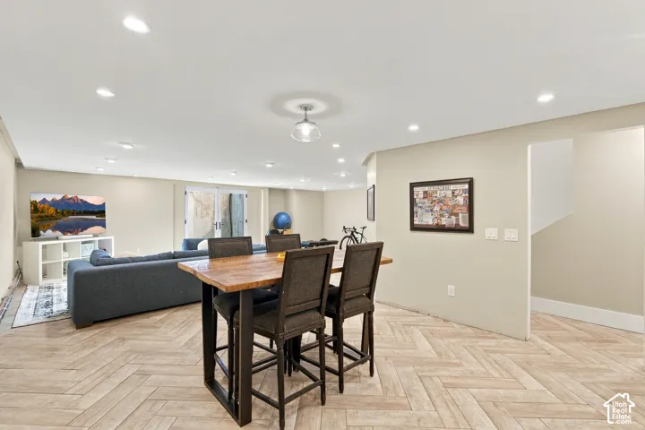Spacious interior featuring wood-finish flooring in a herringbone pattern, recessed lighting, a central pendant light fixture, and double glass-paned doors