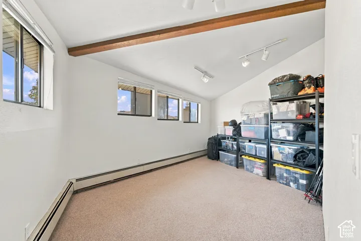 Vaulted ceiling featuring exposed wood beams, neutral carpeting, and multi-directional track lighting
