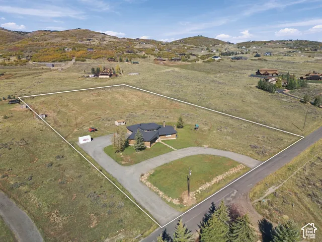 Expansive acreage featuring a multi-faceted roofline, stone exterior accents, a paved circular driveway, and mountainous terrain