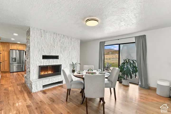 Floor-to-ceiling stone-clad fireplace, wood-finish flooring, built-in stainless steel refrigerator, and glass sliding door