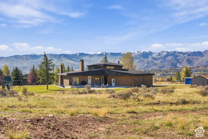 Multi-level brick exterior with dual masonry chimneys, concrete patio, and backdrop of snow-capped mountain range
