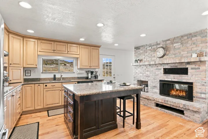 Kitchen featuring light-finish cabinetry, a contrasting central island, stone-surfaced countertops, wood-finish flooring, and a floor-to-ceiling brick fireplace