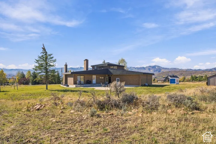Single-story brick residence featuring a multi-faceted roofline, dual exterior chimneys, a concrete patio, and mountain scenery