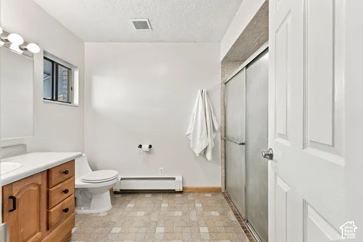 Bathroom featuring a wood-finish vanity with a light-toned countertop, a multi-light fixture, textured tile flooring, and a sliding glass shower door