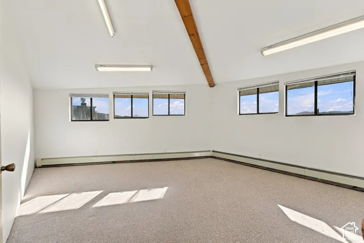Vaulted ceiling featuring an exposed wood beam, neutral carpeting, and multiple windows