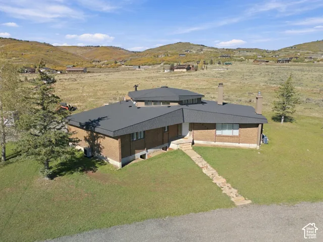 Mid-century modern brick exterior featuring a multi-faceted roofline, clerestory windows, dual masonry chimneys, and a stone walkway set against a mountainous backdrop