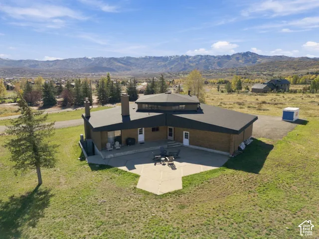 Multi-faceted exterior featuring brick construction, a prominent masonry chimney, a sprawling concrete patio, and a mountain range backdrop