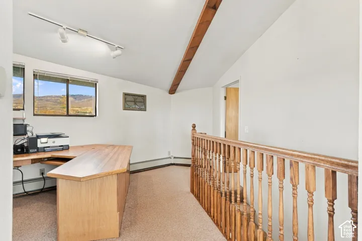 Vaulted ceiling featuring an exposed wood beam, built-in wooden desk, track lighting, and decorative wooden railing