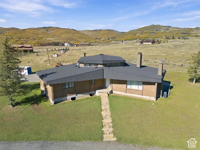 Mid-century modern architectural design featuring a brick exterior, multi-faceted roofline, clerestory windows, dual exterior chimneys, and a stone slab walkway set against a mountainous backdrop