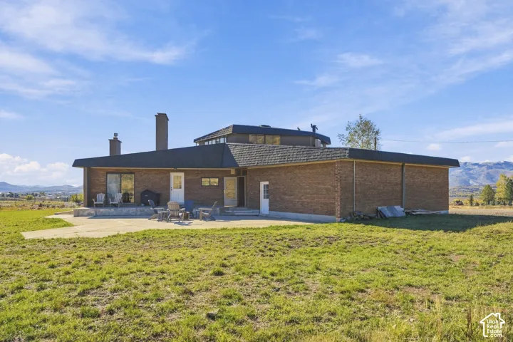 Multi-level brick exterior featuring a sprawling concrete patio, multiple exterior chimneys, and a prominent mountain backdrop