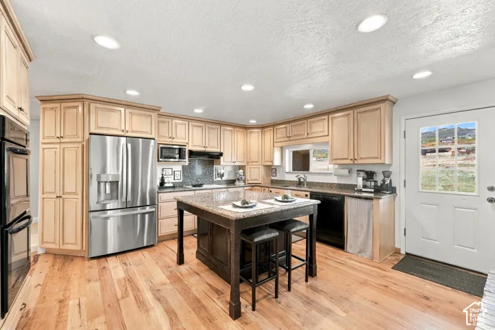 Kitchen featuring light wood cabinetry, stone countertops, a dark-finish center island, recessed lighting, and wood-finish flooring