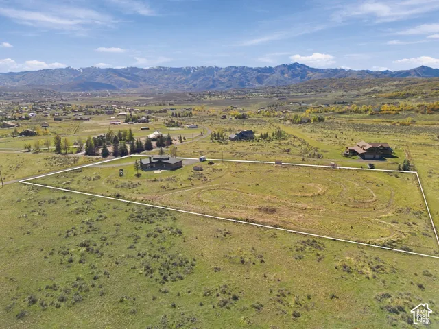 Aerial perspective of a sprawling property featuring extensive open acreage, a single-family residence, and prominent mountain backdrops