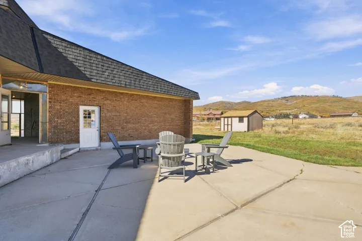 Concrete patio featuring a brick exterior facade, a storage shed, and a mountainous landscape backdrop