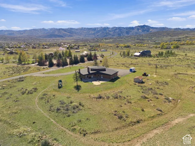 Aerial perspective of a detached residence featuring a paved patio, detached storage shed, gravel driveway, and prominent mountain backdrop