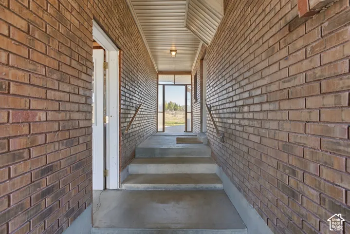 Covered entryway featuring full-height brick masonry walls, concrete steps, and a built-in metal handrail