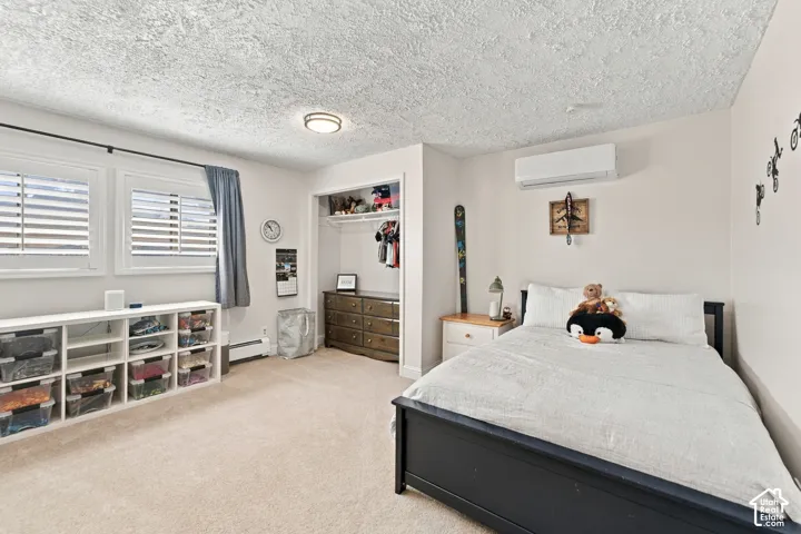 Bedroom featuring carpeted flooring, wall-mounted ductless heating and cooling unit, closet with built-in shelving, and white plantation-style window shutters