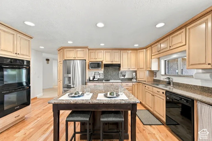 Kitchen featuring wood-finish cabinetry, stone countertops, central island, wood-finish flooring, and stainless steel double wall ovens