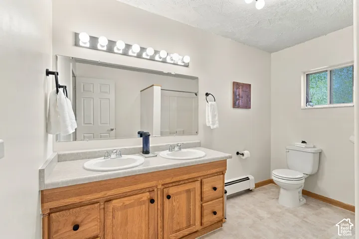 Bathroom vanity featuring dual inset sinks, light-toned countertop, wood cabinetry with dark hardware, a full-width wall mirror, and a multi-bulb light fixture