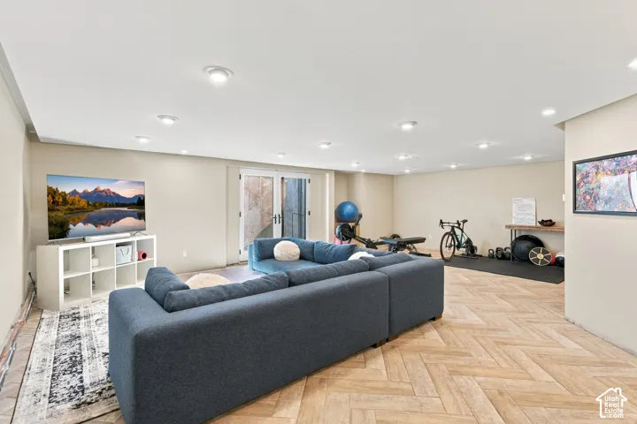 Open-concept room featuring wood-finish flooring in a herringbone pattern, recessed lighting, and glass-paneled double doors providing exterior access