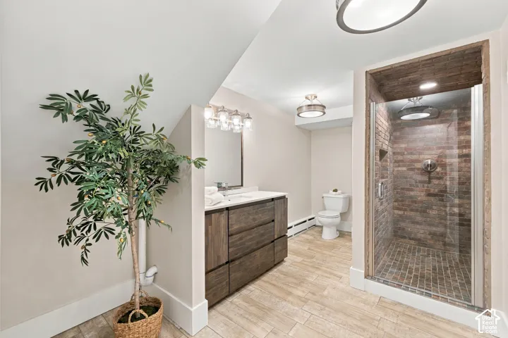 Bathroom featuring a wood-finish vanity with a stone countertop, tile flooring, and a walk-in shower with exposed brick interior and glass enclosure