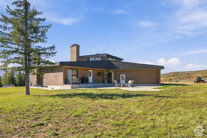 Mid-century modern brick exterior featuring a concrete patio, tall masonry chimney, tiered roofline, and expansive grounds