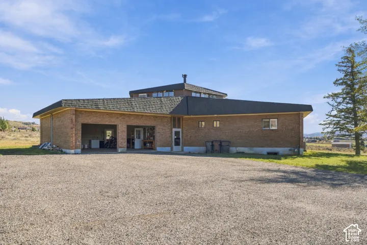 Multi-level brick exterior featuring a multi-faceted roofline, an attached two-car garage, and expansive gravel driveway