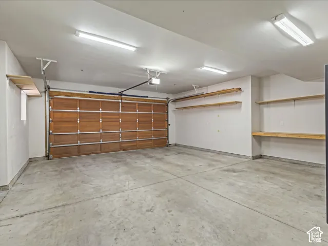 Multi-car garage featuring a sectional wood-finish door, concrete flooring, overhead fluorescent lighting, and extensive built-in wall shelving