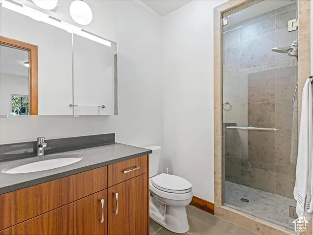 Bathroom featuring a wood-finish vanity with a stone-composite countertop, integrated sink, mirrored medicine cabinet, and a walk-in shower with stone tile surround and frameless glass door