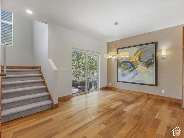 Wood-finish flooring, recessed lighting, multi-tiered chandelier, staircase with carpeted treads and wood handrail, and sliding glass door