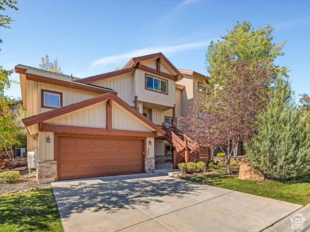 Multi-level exterior featuring vertical wood-style siding, stone masonry accents, a paved driveway, and an attached two-car garage