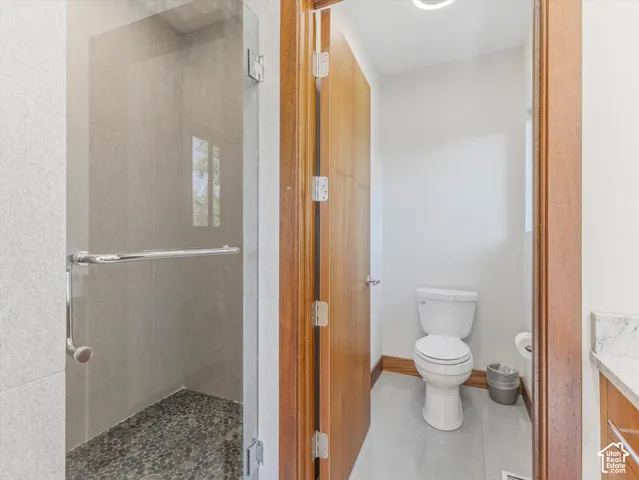 Glass-enclosed shower with stone-tile surround and river-rock flooring, natural wood door, and stone-surfaced vanity