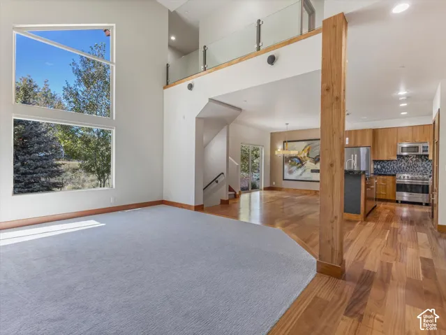 Floor-to-ceiling windows, wood-finish flooring, exposed natural wood support column, glass panel railing on the upper level, and kitchen cabinetry with integrated stainless steel appliances