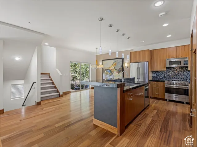 Kitchen featuring wood-finish cabinetry, a kitchen island with stone countertops, stainless steel appliances, a tiled backsplash, and wood-finish flooring