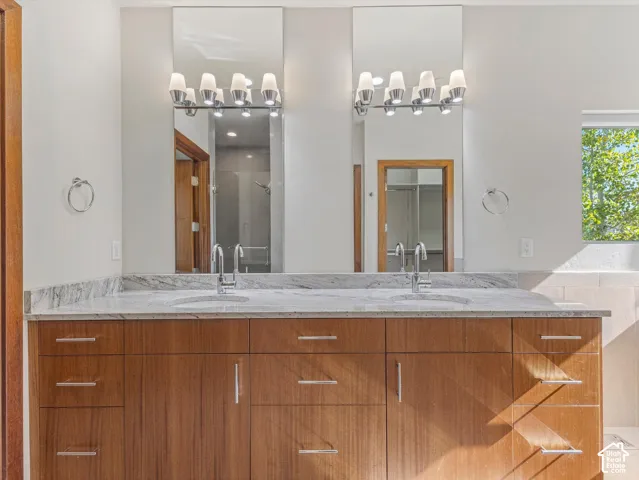 Dual-sink vanity featuring a stone countertop, wood-finish cabinetry, two full-length mirrors, and multi-light fixtures