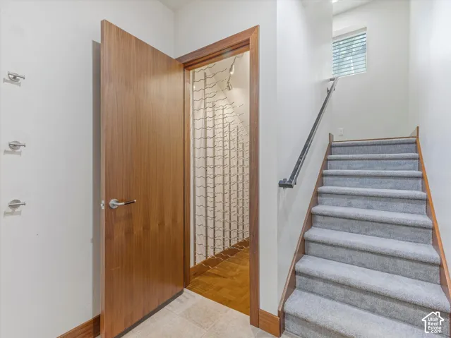 Custom wood-finished door, built-in metal wine storage racking, carpeted staircase with a metal handrail, and recessed lighting