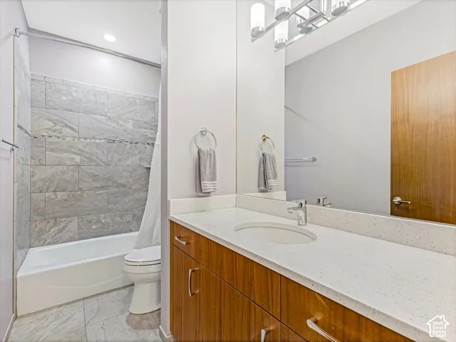 Bathroom featuring wood-finish cabinetry, a solid-surface vanity countertop with an integrated basin, a large wall-mounted mirror, and a tub-shower combination with floor-to-ceiling tile surround