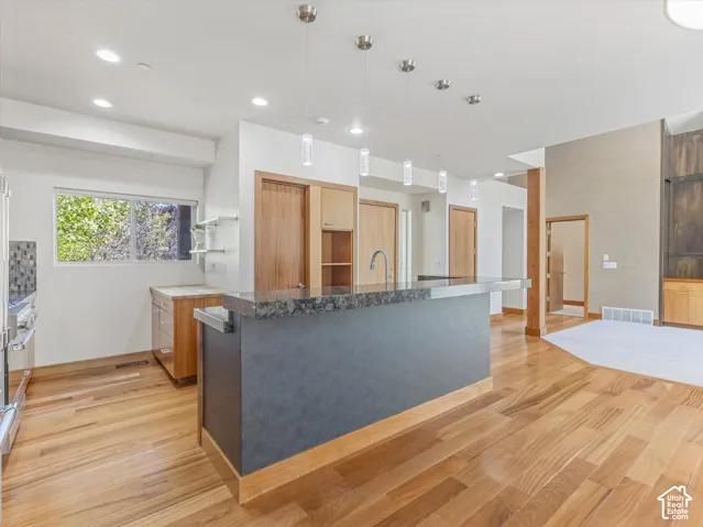 Kitchen featuring a dark stone-finish breakfast bar, wood-finish flooring, series of four glass pendant lights, and natural wood cabinetry