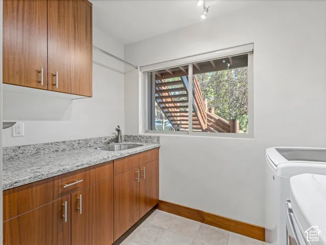 Laundry area featuring wood-finish cabinetry, stone-surface countertops, an integrated stainless steel sink with a high-arch faucet, and tile flooring
