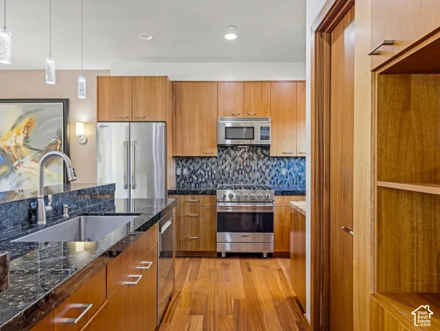 Modern kitchen featuring warm wood cabinetry, stainless steel appliances, and a blue-toned tile backsplash
