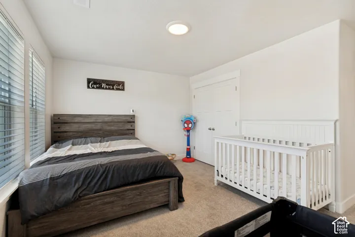 Carpeted bedroom with white walls, dual windows with horizontal blinds, a white ceiling light fixture, and a white bi-fold closet door