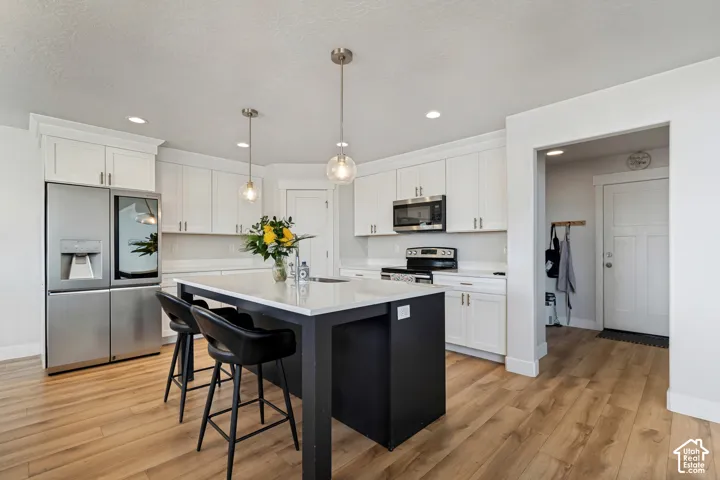 Kitchen featuring light wood-finish flooring, white cabinetry, a black kitchen island with a white countertop, and stainless steel appliances