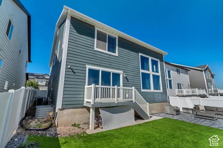 Exterior featuring blue siding, a white fenced yard, a paver patio, a small deck with white railings, and large multi-pane windows