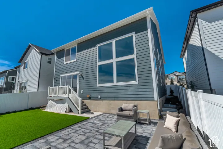 Paved patio area, artificial turf lawn, white vinyl fencing, exterior siding, and a wooden deck with stairs
