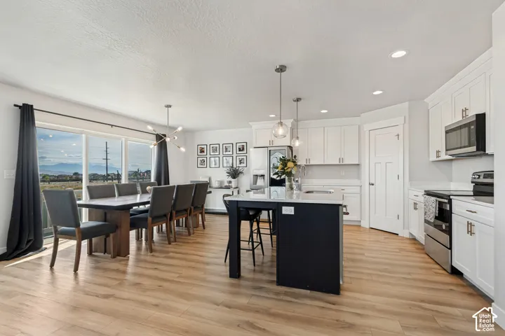 Open-concept room featuring wood-finish flooring, white cabinetry, a kitchen island with a light-toned countertop, and stainless steel appliances