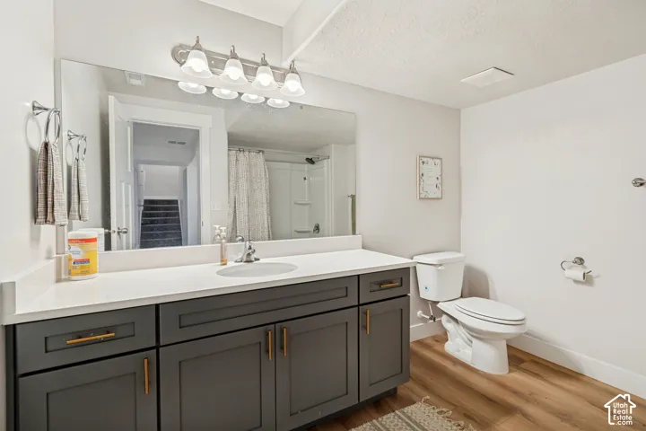 Bathroom featuring a dual-sink vanity with a white countertop, dark cabinetry, modern hardware, and wood-finish flooring